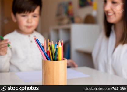 Little preschooler kid drawing with coloured pencils with mother or teacher educator. Focus on the pencils. Homeschooling. Learning community. Montessori school.