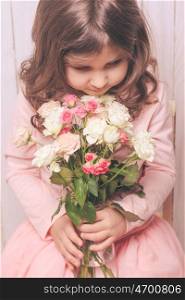 Little pretty girl in pink holds the bouquet of roses. Close up the flowers and face. Girl with roses