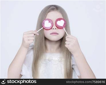 little pretty girl with big candy. Studio ashion photography of kid in white dress. Beautiul model eating sweet lollipop.