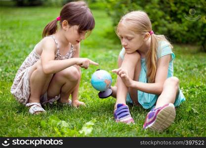 little pretty girls girlfriends sitting on the lawn and look at the globe