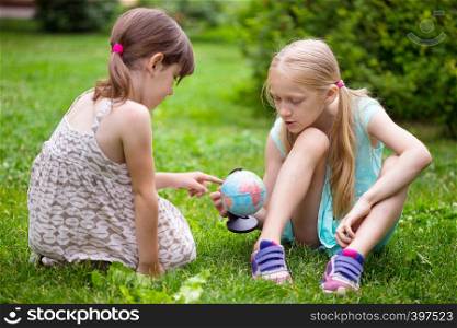 little pretty girls girlfriends sitting on the lawn and look at the globe