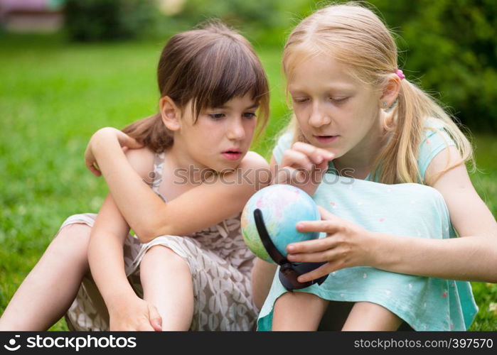 little pretty girls girlfriends sitting on the lawn and look at the globe