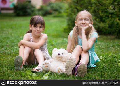 little pretty girls girlfriends sitting on the lawn with his toy teddy bear. Happy summer
