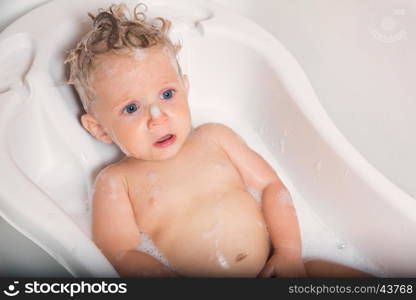 Little pretty wet baby boy in bath room sitting and sad on white background, horizontal picture.