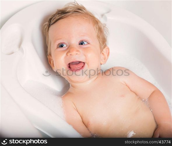 Little pretty wet baby boy in bath room sitting and smiling on white background, horizontal picture.