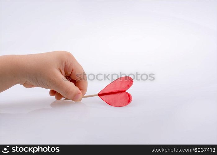 Little red color heart shape at the top of a stick in hand