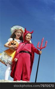 Little Red Devil holding a pitchfork and Cute Happy Witch holding Jack O&rsquo; Lantern, Standing at the Blue Sky.