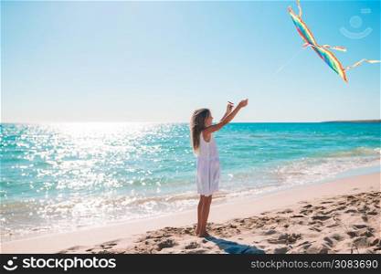 Little running girl with flying kite on tropical beach. Little girl flying a kite on beach at sunset