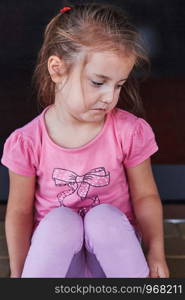 Little sad girl crying because of lost her toy, sitting on a step on the patio. Real people, authentic situations