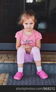 Little sad girl crying because of lost her toy, sitting on a step on the patio. Real people, authentic situations
