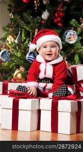 Little Santa boy sitting on a gift boxes.