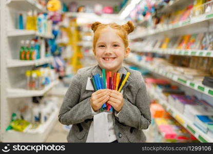 Little school girl holds colorful markers, shopping in stationery store. Female child buying office supplies in shop, schoolchild in supermarket. School girl holds markers, stationery store