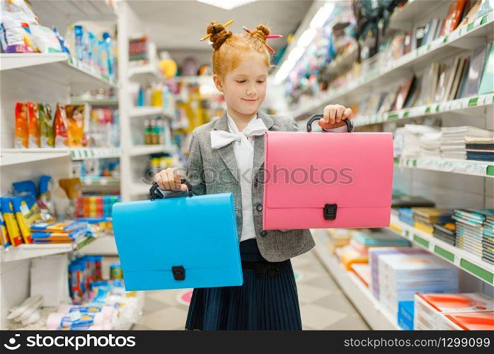Little school girl with two folders in stationery store. Female child buying office supplies in shop, schoolchild in supermarket. School girl with two folders in stationery store