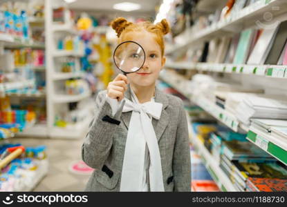 Little schoolgirl choosing magnifying glass, shopping in stationery store. Female child buying office supplies in shop, schoolchild in supermarket