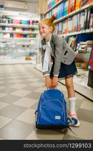 Little schoolgirl with heavy school backpack at the shelf in stationery store. Female child buying office supplies in shop, schoolchild in supermarket