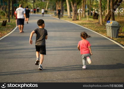 Little sister girl and older brother boy run together on park running track, sun light. Concept of happy family sport for healthy lifestyle. Back view.