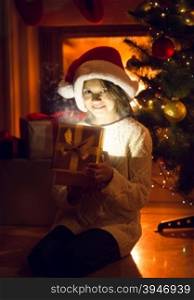 Little smiling girl holding sparkling present under Christmas tree