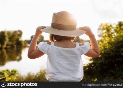 Little smiling girl in straw hat is having fun on summer holiday vacations. Happy child playing by the lake. Kid having fun outdoors. healthy lifestyle concept. back view.. Little smiling girl in straw hat is having fun on summer holiday vacations. Happy child playing by the lake. Kid having fun outdoors. healthy lifestyle concept. back view