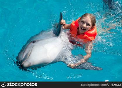 Little Smiling Girl Swimming with the Dolphin in the Swimming Pool in the Bright Sunny Day