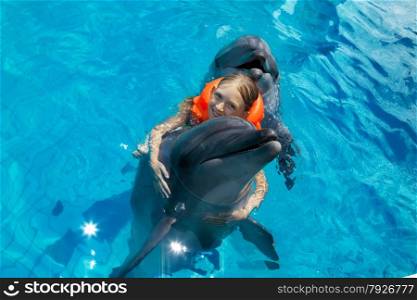 Little Smiling Girl Swimming with the Dolphin in the Swimming Pool in the Bright Sunny Day