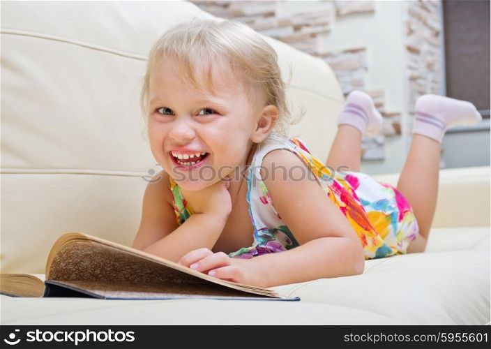 Little smiling girl with book on sofa