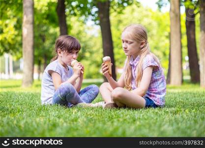 little smiling girls girlfriends sitting on the lawn and eating ice cream. children's holidays