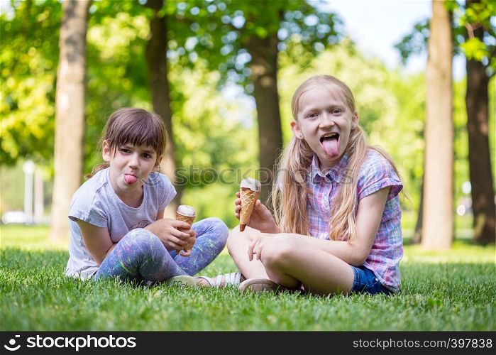 little smiling girls girlfriends sitting on the lawn and eating ice cream. children's holidays