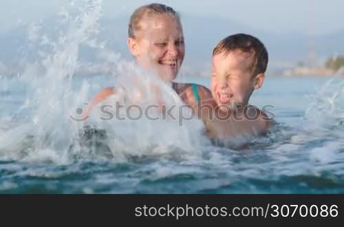 Little son and mother fooling in sea splashing it with all their might. Family fun in the water