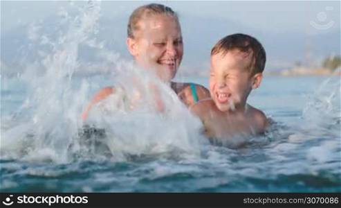 Little son and mother fooling in sea splashing it with all their might. Family fun in the water
