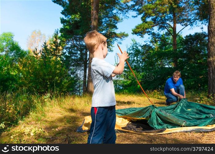 little son helps to establish a tent on the nature
