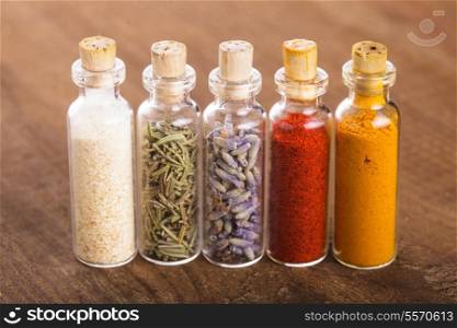 Little souvenir bottles with spices over wooden table. Celerey, rosemary, lavender, paprika, turmeric