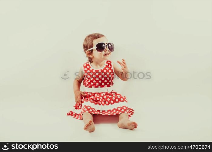 Little stylish girl in a red polka-dot dress and glasses posing for photos. Girl in retro