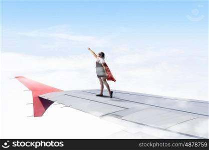Little super hero. Powerful super hero kid girl standing on wing of flying airplane