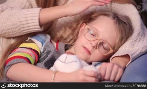 Little teenager girl with teddy bear falling asleep on mother&acute;s lap. Mother gently caressing her beautiful daughter while she is falling asleep. Focus on little girl face and mother&acute;s arm close up.