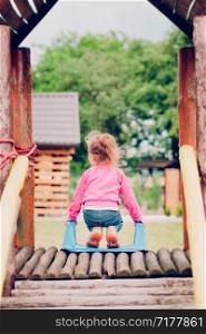 Little toddler girl playing in the playground standing on slide