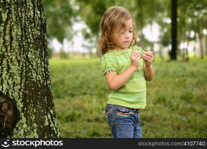 Little toddler girl playing on the park with a green leaf