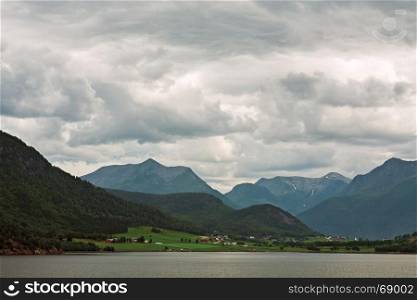 Little village and mountains along the Romsdalsfjorden near Andalsnes under a cloudy sky, Norway. Along the Romsdalsfjorden near Andalsnes, Norway
