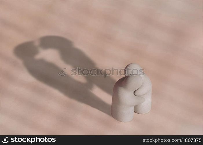 Little white terracotta garden figurine in hug gesture with long shadow of couple kissing together on pink tile floor background, love concept