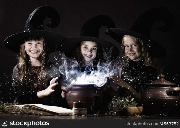 Little witches. Three little Halloween witches reading spell above pot