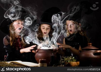 Little witches. Three little Halloween witches reading spell above pot