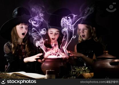 Little witches. Three little Halloween witches reading spell above pot