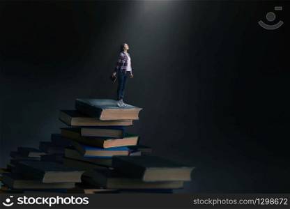 Little young woman standing on mountain of large books and textbooks, scale effect. Knowledge and education, reaiding concept