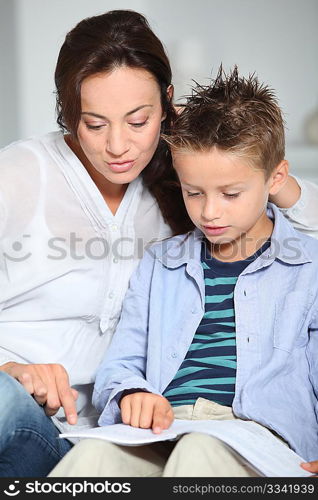 Littme boy and mother sitting on sofa at home with book