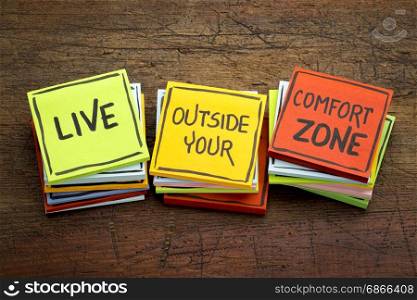 Live outside your comfort zone - motivational handwriting in black ink on sticky notes against rustic wood