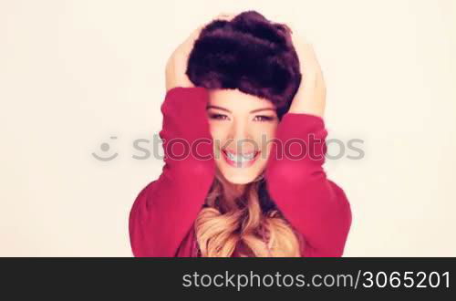 Lively Woman In Fur Hat with her hands to the earflaps laughing at the camera.