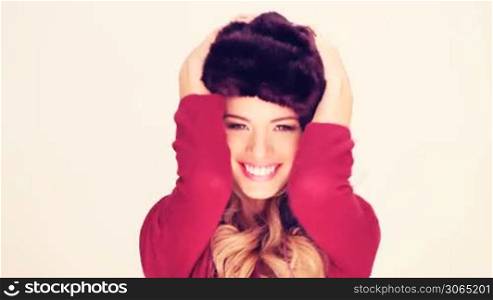 Lively Woman In Fur Hat with her hands to the earflaps laughing at the camera.