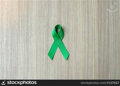 Liver Cancer Awareness, green Ribbon on wooden background for supporting people living and illness. Healthcare and World cancer day concept