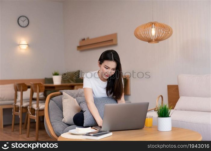 Living room concept in the coffee shop a girl with a bun hair using her laptop going on the internet with a glass of orange juice.