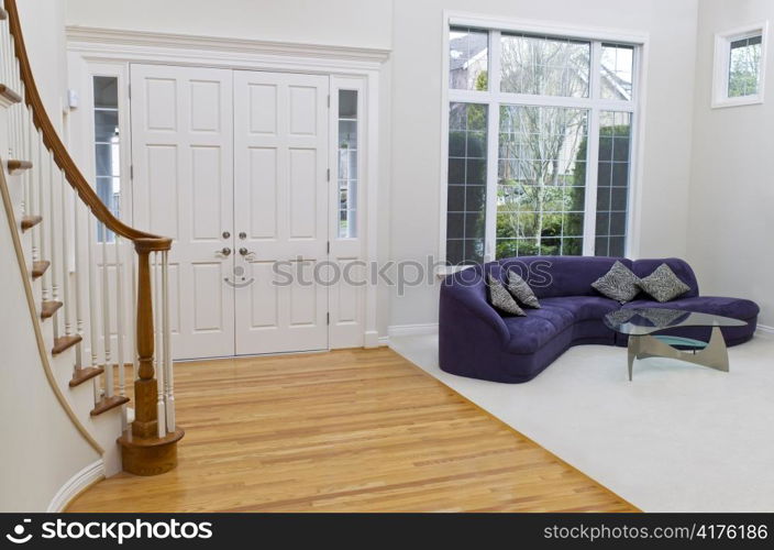 Living room with sofa, glass table, oak and carpet floors with large window in background