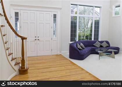 Living room with sofa, glass table, oak and carpet floors with large window in background